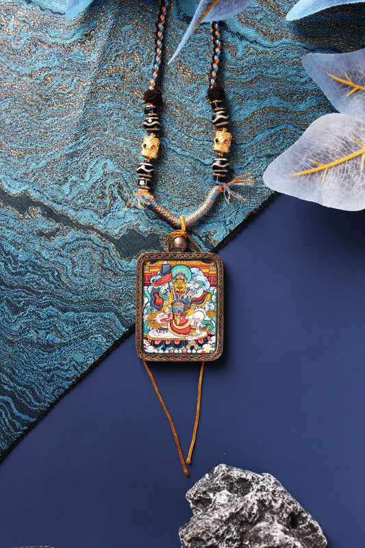 Front close-up of Vaishravana thangka pendant featuring vivid mineral pigment colors, detailed linework and traditional iconography, mounted in a Dunhuang Nine-Color Deer sterling silver protective frame with hanging cord and tassels