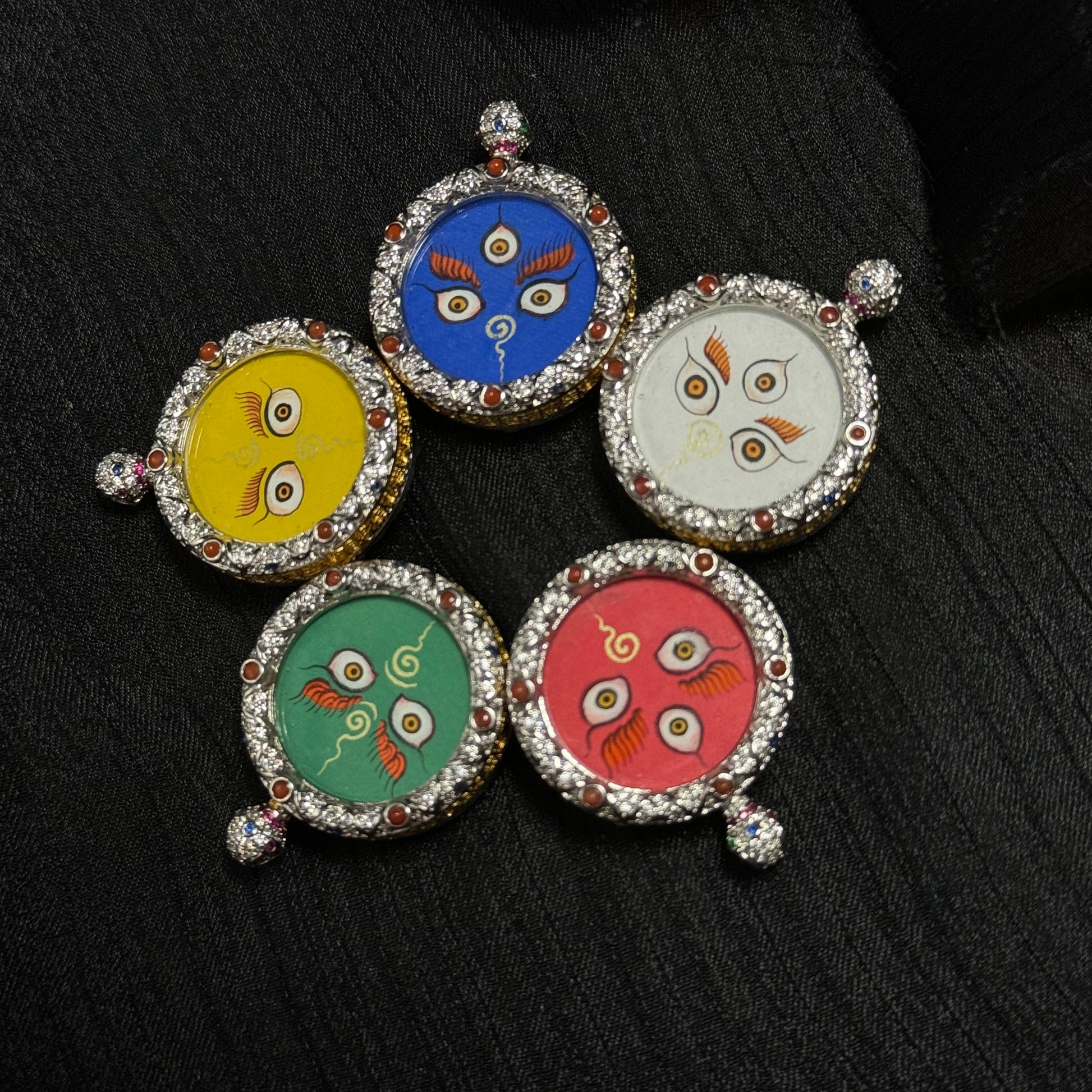 Close-up detail of a Five Jambhala wealth eye thangka pendant showing hand-painted sacred eye motif on mineral pigment background with jeweled copper frame.