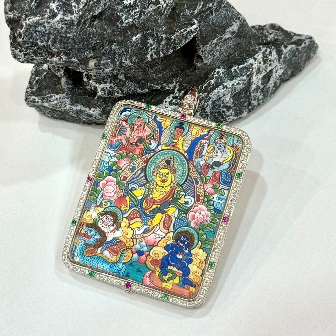 Front display of Five Jambhala pendant on a wooden tray, highlighting the full five-deity composition, detailed floral background, and the silver case border with sparkling colored accents.