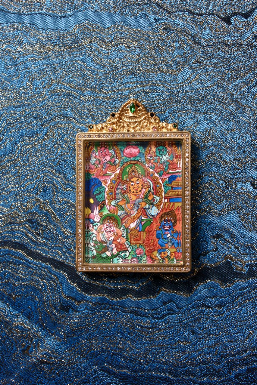 Front view of Five Wealth Deities mini thangka pendant centered on textile background, hand-painted mineral pigment artwork in jeweled double-sided titanium steel case, Nepal series