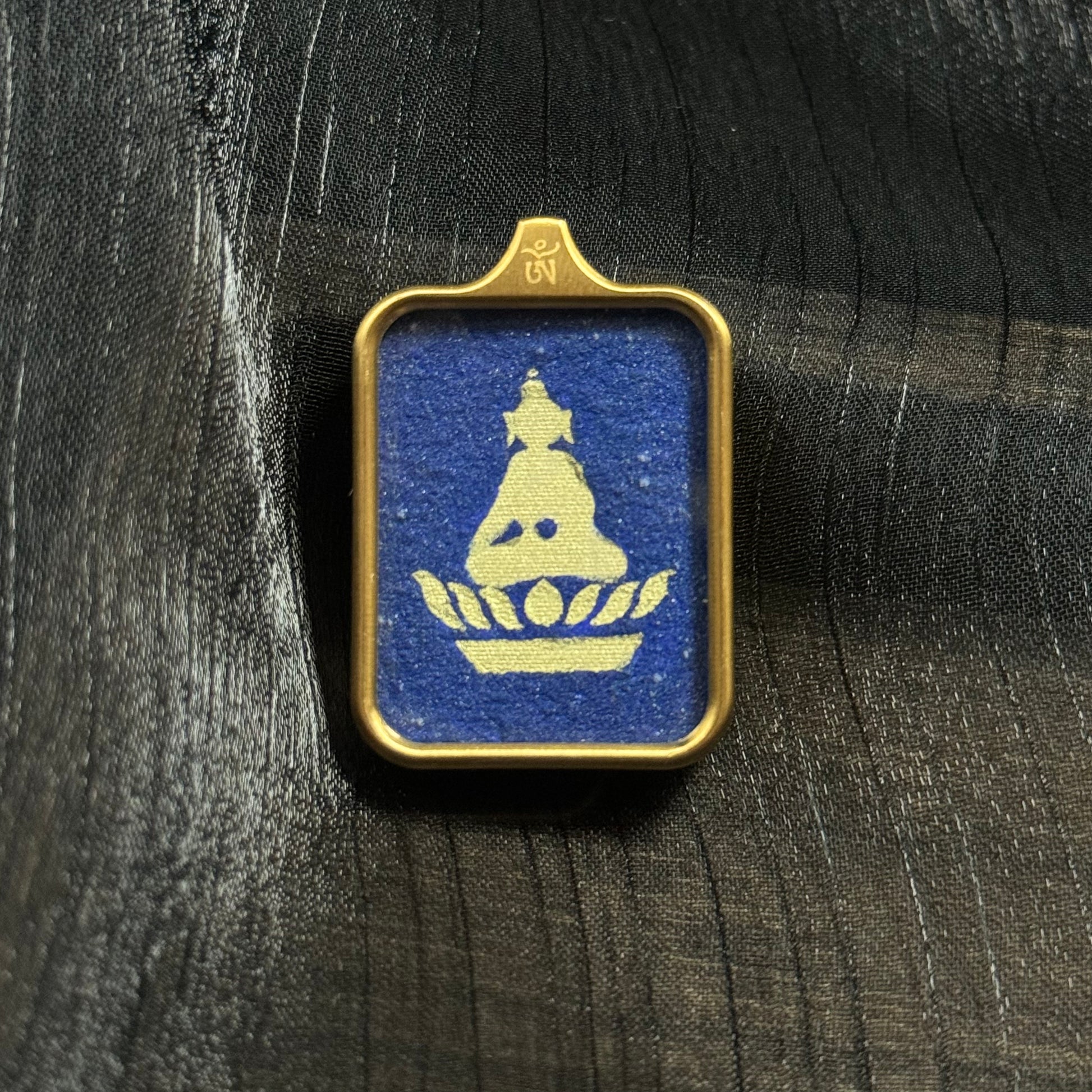 Hand-painted Formless Buddha mini thangka pendant from Rebgong featuring a minimalist Buddha silhouette painted with gold powder on a deep blue lapis lazuli mineral pigment background inside a rectangular metal frame.