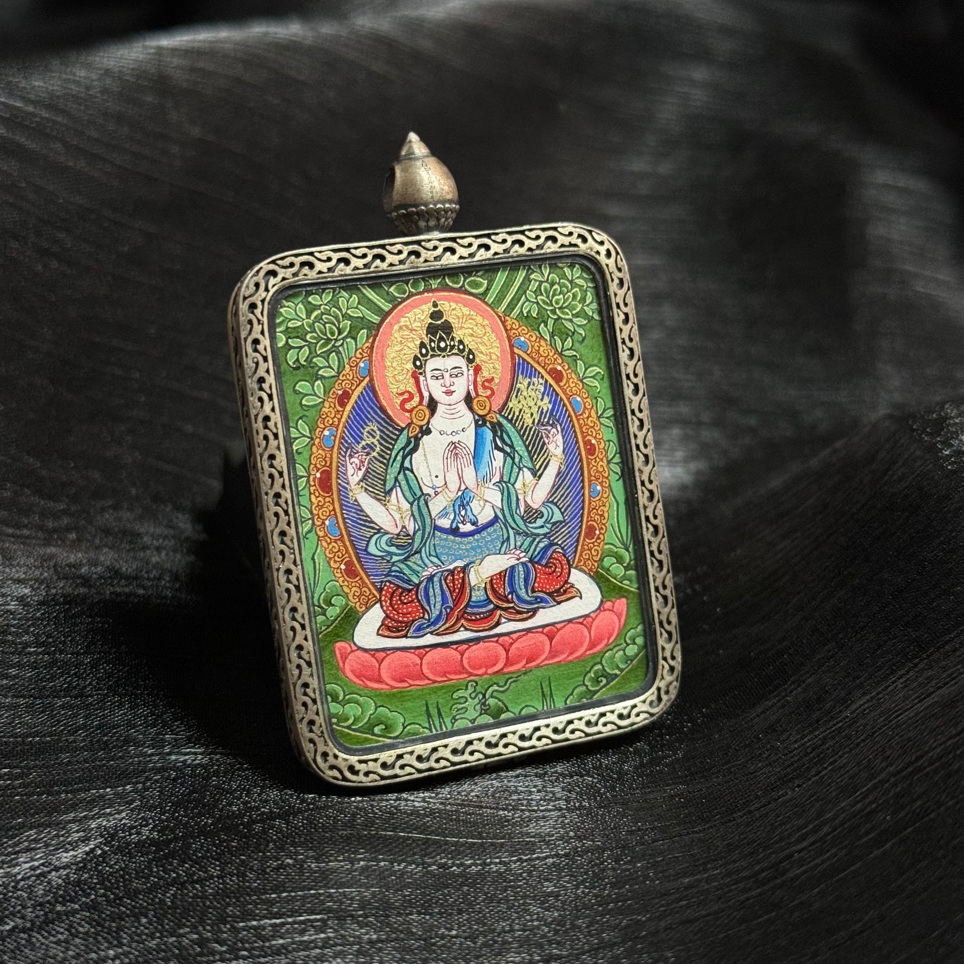 Front view of Four-Armed Avalokiteshvara Chenrezig mini thangka pendant showing hand-painted Rebgong thangka artwork with mineral pigments and decorative metal frame
