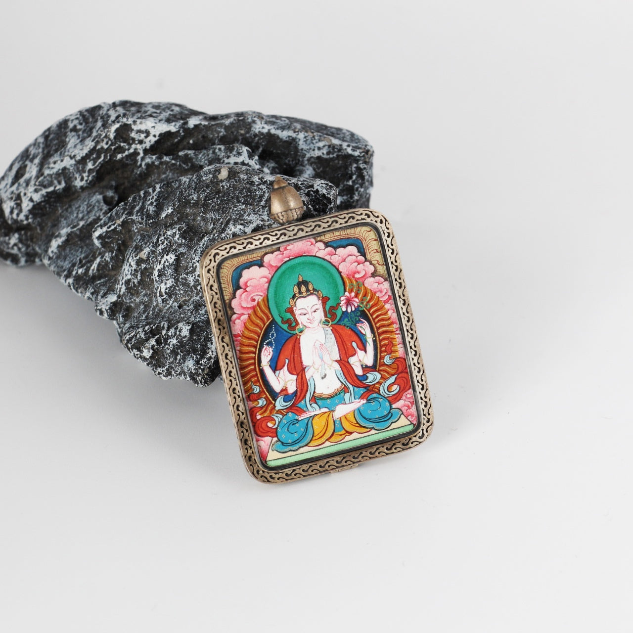 Angled view of the Four-Armed Avalokiteshvara mini Thangka pendant, highlighting layered mineral pigment colors, refined line work, and the thickness of the silver gawu-style frame.