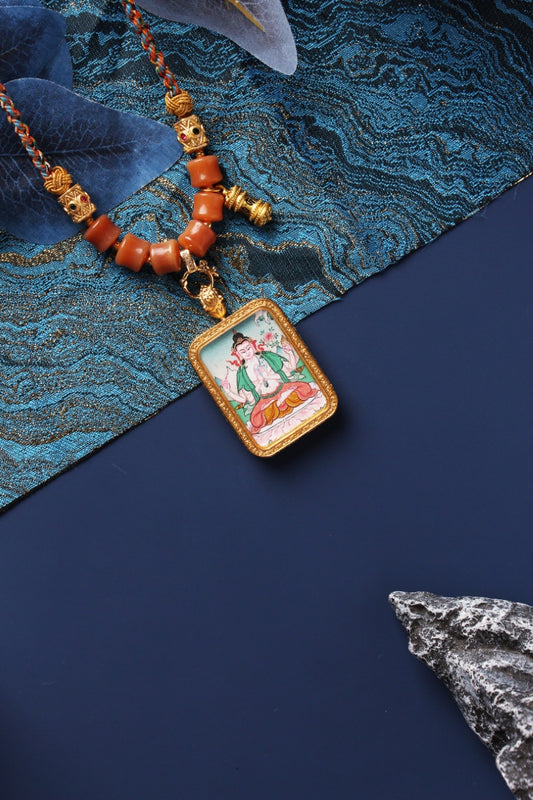 Angled view of Four-Armed Avalokiteshvara mini thangka pendant showing mineral pigment hand-painting, rectangular textured metal bezel, and bead details near the pendant loop