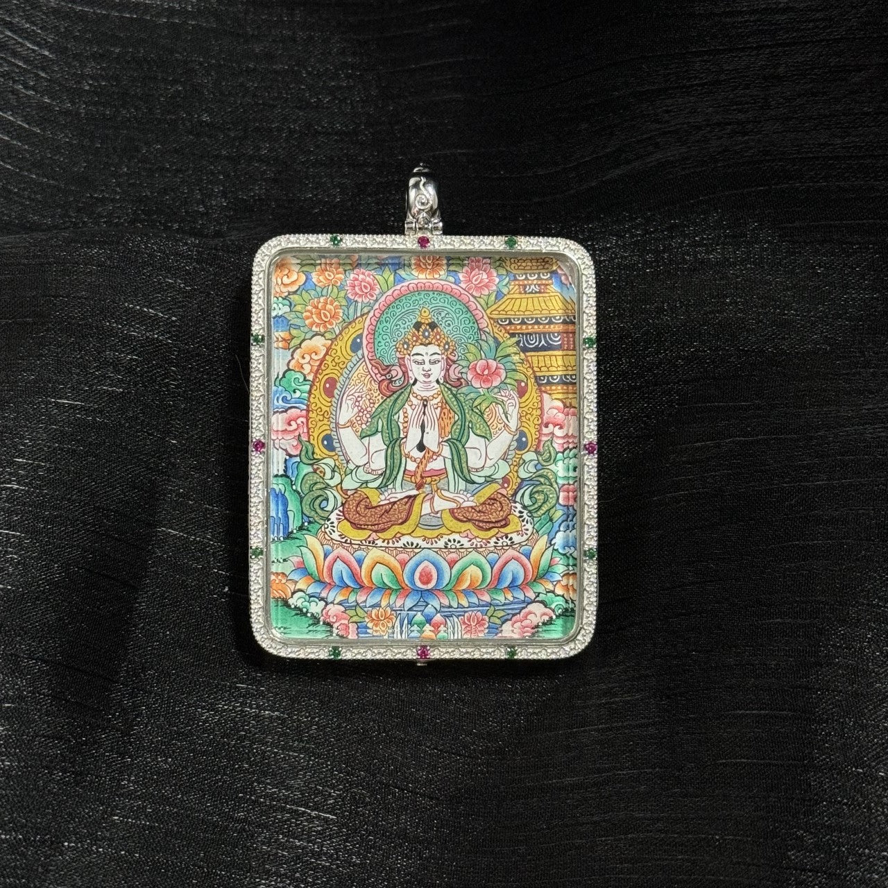 Close-up front view of the Four-Armed Avalokiteshvara mini thangka pendant, showing detailed hand-painted Avalokiteshvara with lotus throne, floral background, and traditional Tibetan iconographic elements inside a 925 silver pendant frame.