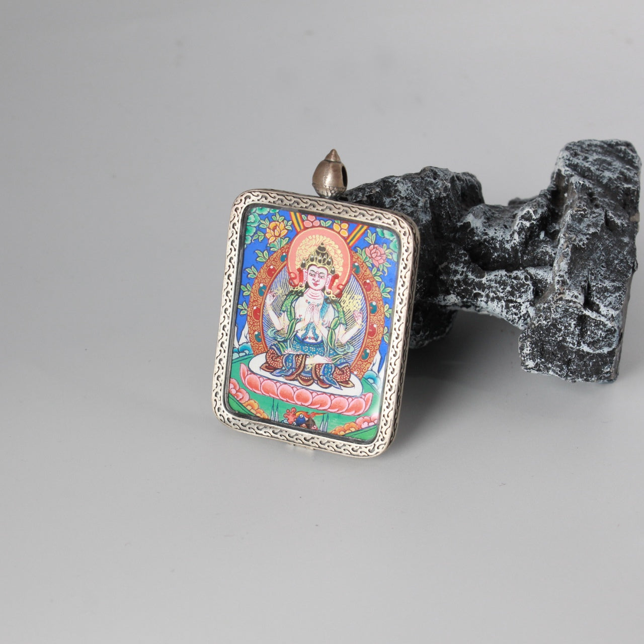 Close view of Four-Armed Avalokiteshvara thangka painting highlighting vivid floral background, halo and lotus seat details, framed in an engraved silver case
