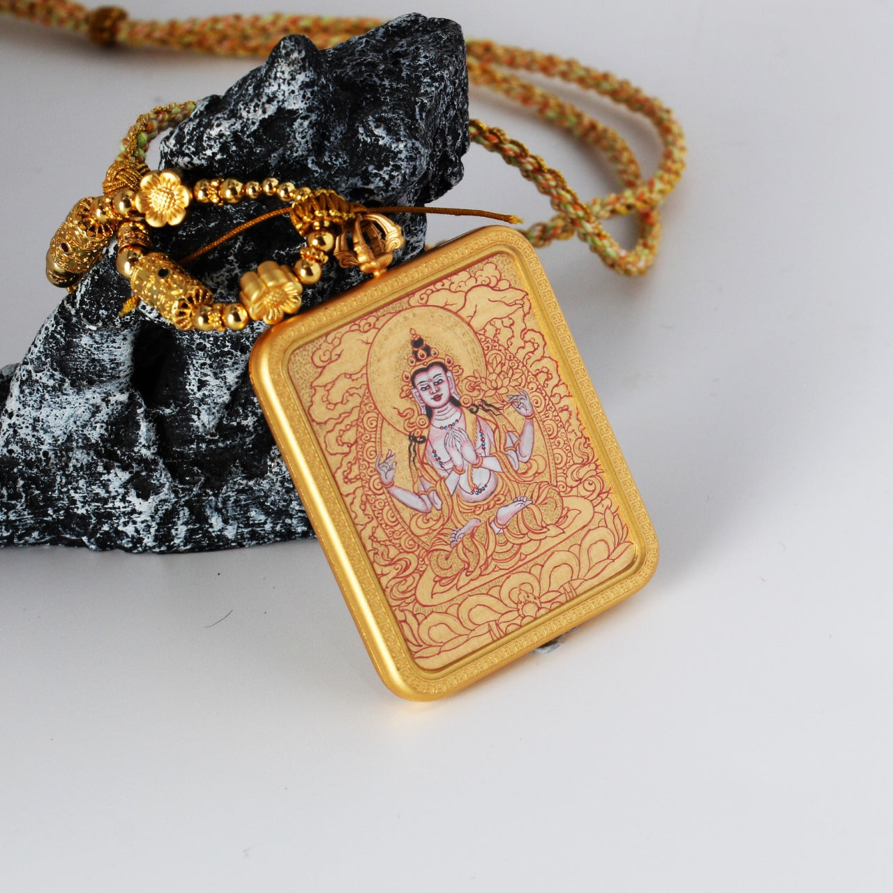Close-up of a Four-Armed Avalokiteshvara mini thangka pendant showing the braided cord, decorative metal beads, and handcrafted hanging structure designed for portable thangka use.