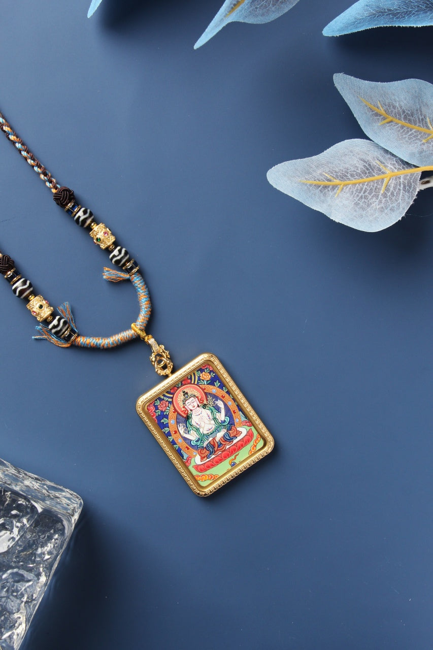Angled front view of the Four-Armed Avalokiteshvara mini thangka pendant showing the hand-painted image, the metallic case edge thickness, border texture, and the clasp-to-bail hardware connection.