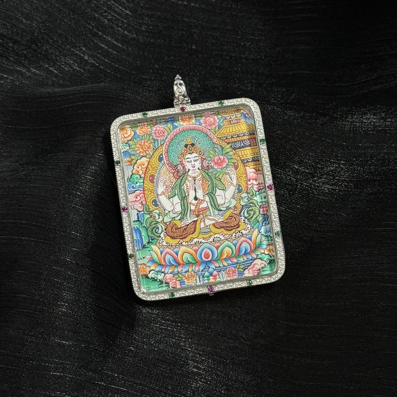 Detailed view of the Four-Armed Avalokiteshvara mini thangka pendant showing the deity seated on a multicolored lotus throne, surrounded by intricate floral motifs and traditional Tibetan decorative patterns within a square silver pendant case.
