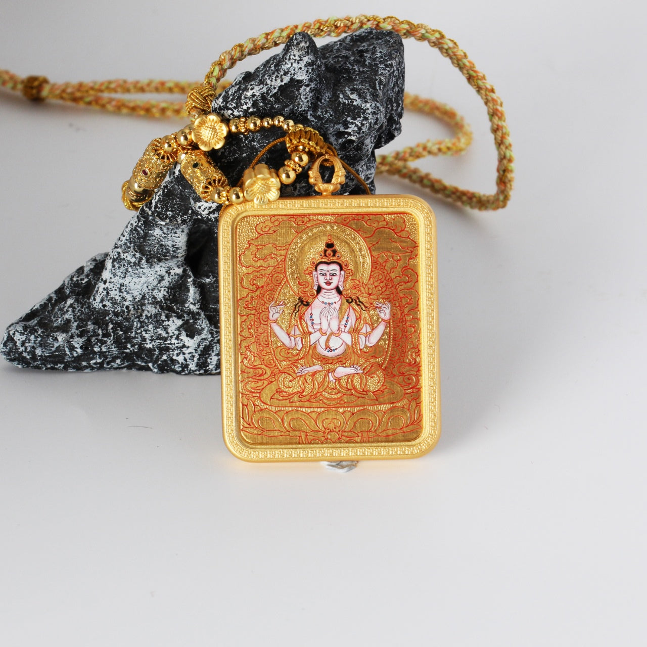 Front view of a Four-Armed Avalokiteshvara mini thangka pendant, hand-painted in Rebgong gold thangka style with mineral pigments, featuring detailed red line work, gold-ground background, and a copper protective case.