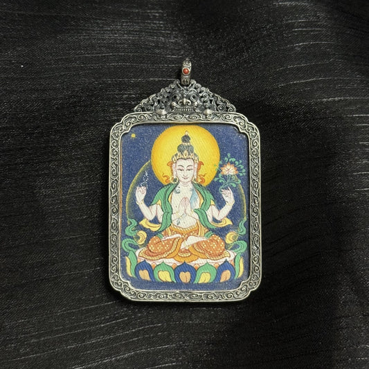Angled view of Four-Armed Avalokiteshvara mini thangka pendant, hand-painted with natural mineral pigments and set in an ornate vintage silver case with carved decorative patterns.