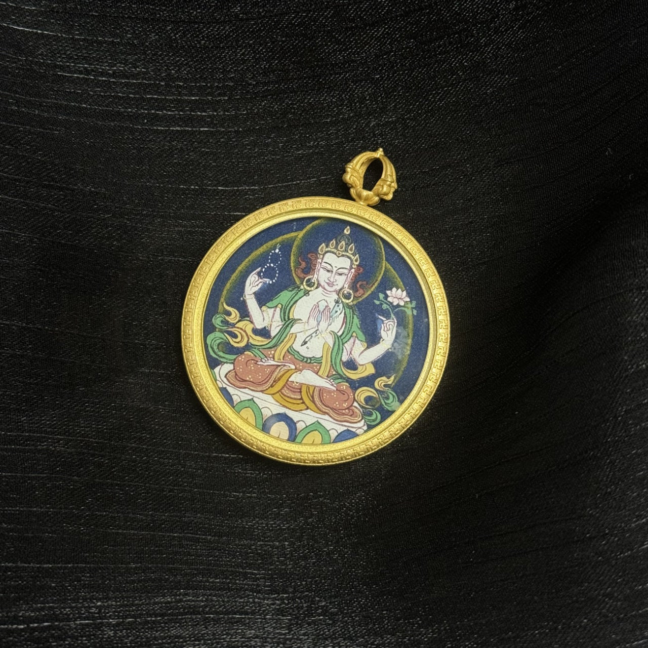 Close-up view of a Four-Armed Avalokiteshvara round mini thangka pendant showing the brass frame, hanging loop, and hand-painted mineral pigment artwork