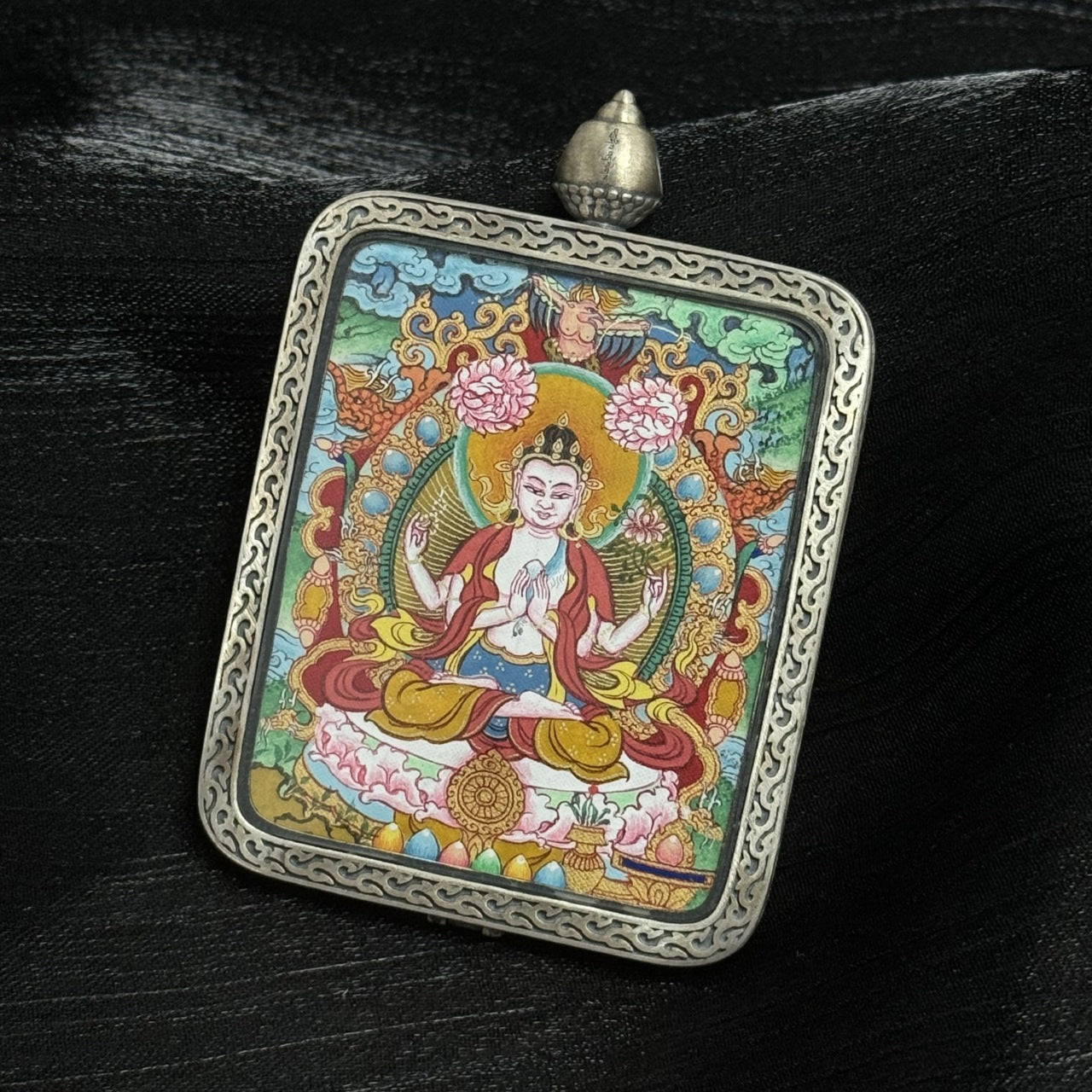 Side perspective of Four-Armed Avalokiteshvara Tibetan Miansa mini thangka pendant emphasizing color saturation, halo structure, lotus platform, and engraved silver border craftsmanship.