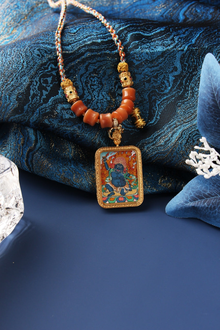 Front view of Acalanatha mini thangka pendant featuring a blue wrathful deity with flame background, set in a rectangular metal frame with beaded necklace components