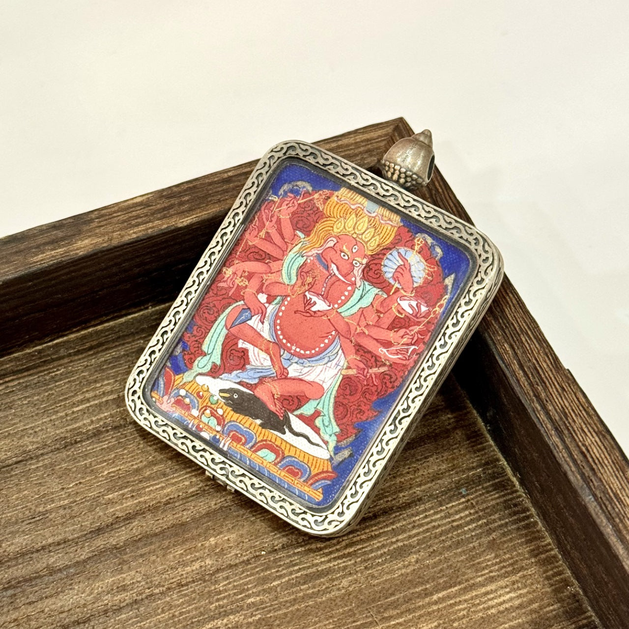 Angled view of Ganapati (Vinayaka) mini thangka pendant showing the thickness and texture of the pure silver case, engraved border design, and the hand-painted red deity image.