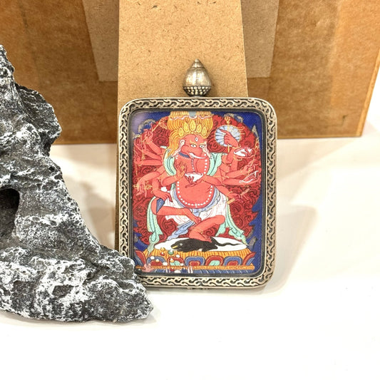 Front view of Ganapati (Vinayaka) mini thangka pendant showing a red multi-armed elephant-headed deity with flame halo and blue background, set in an ornate pure silver case with patterned border.