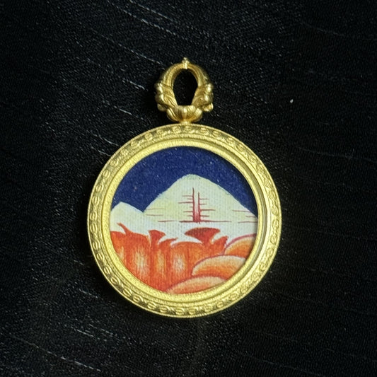 Close-up of “Golden Sunlight” Mount Kailash pendant, white snow peak with red-orange sunlit mountains, blue sky background, detailed copper border and bail