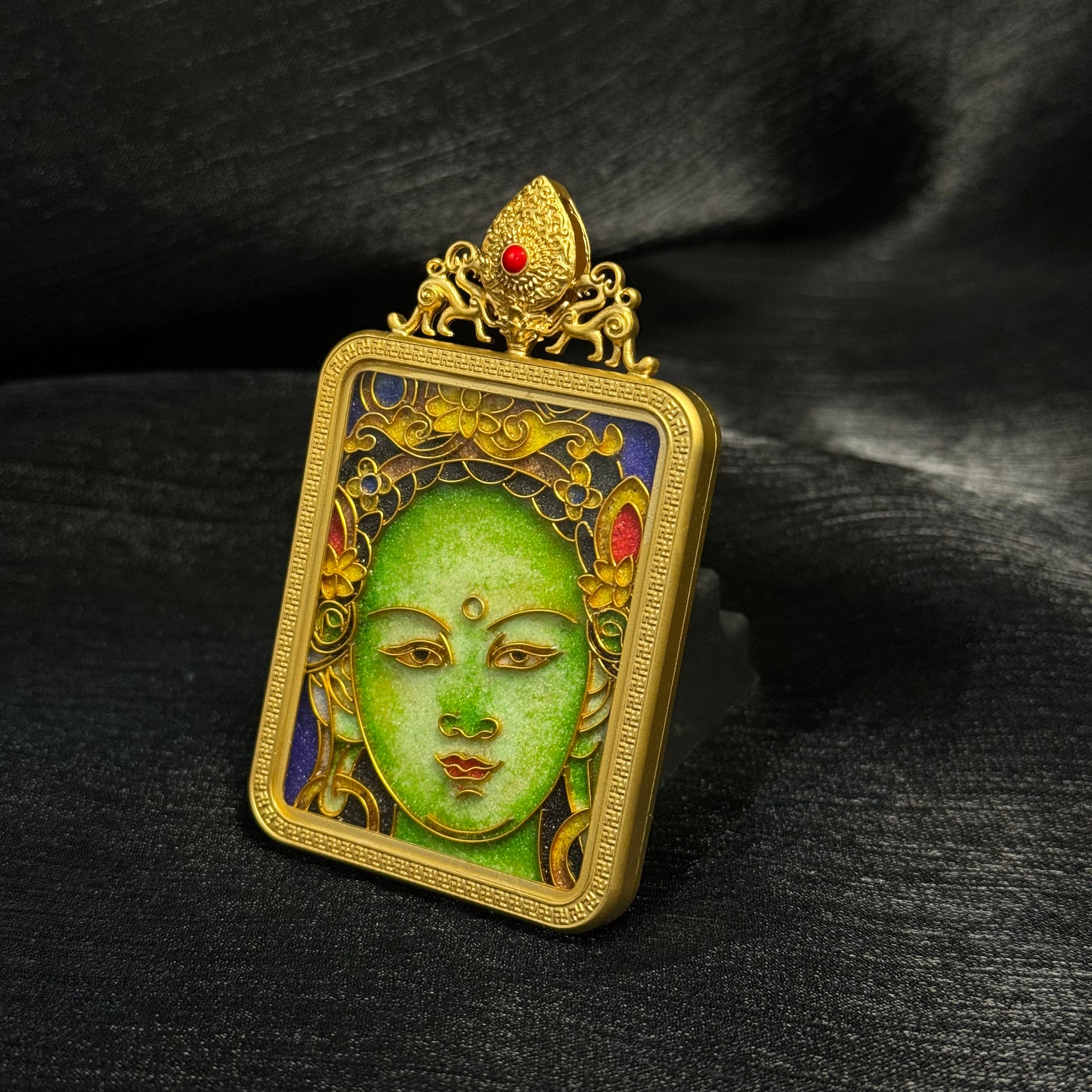 Angled view of handcrafted Green Tara cloisonné enamel pendant highlighting raised enamel details, gold-plated copper frame, and decorative crown element.