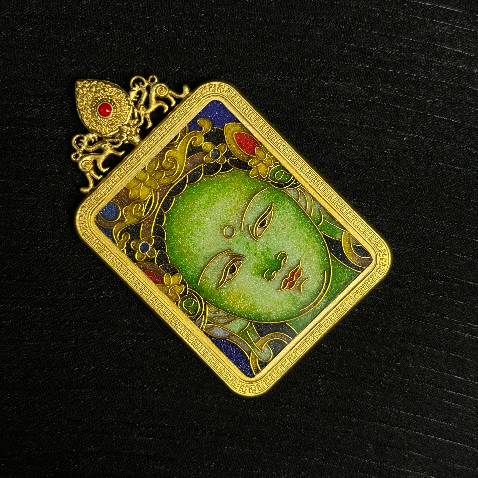 Detailed view of Green Tara cloisonné enamel pendant showing facial expression, gold wire cloisonné patterns, and textured enamel background.