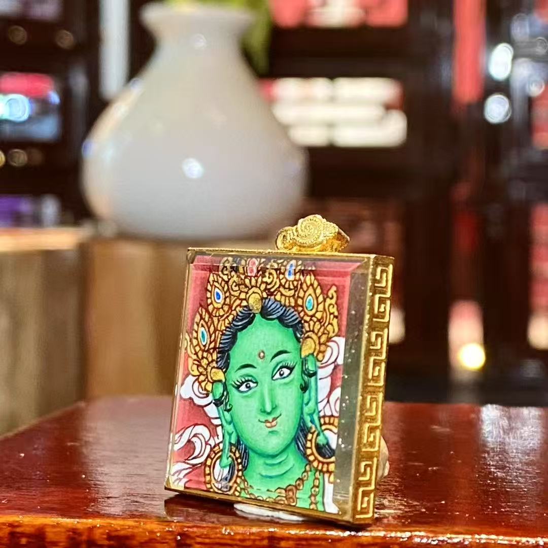 Side view of a Green Tara Gau Thangka pendant showing the slim 18K gold frame, double-sided sapphire crystal, and fine miniature craftsmanship