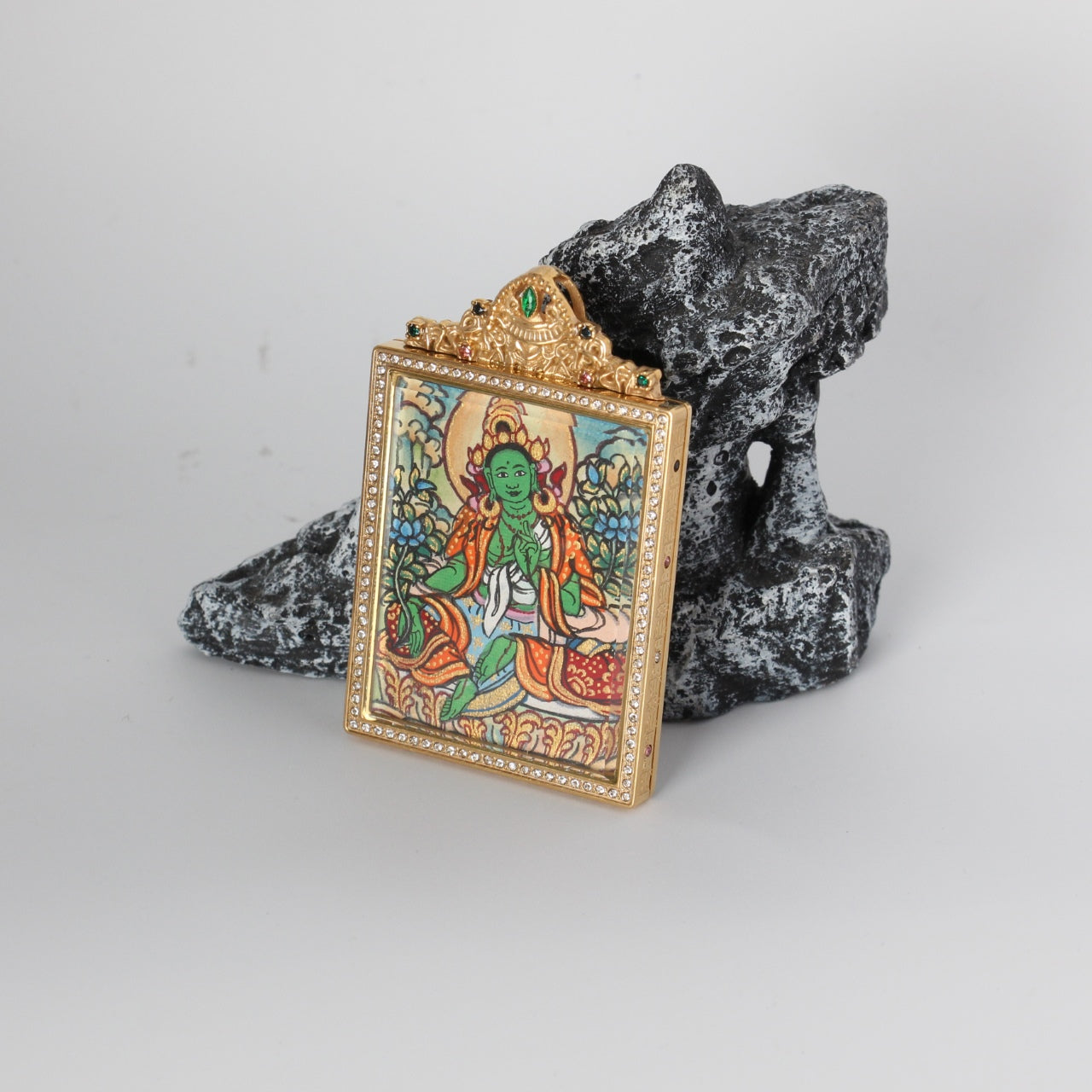 Angled view of the Green Tara mini thangka pendant highlighting the crystal-set border around the frame, the gold-tone case depth, and the ornate crown top with green and multicolor stones.
