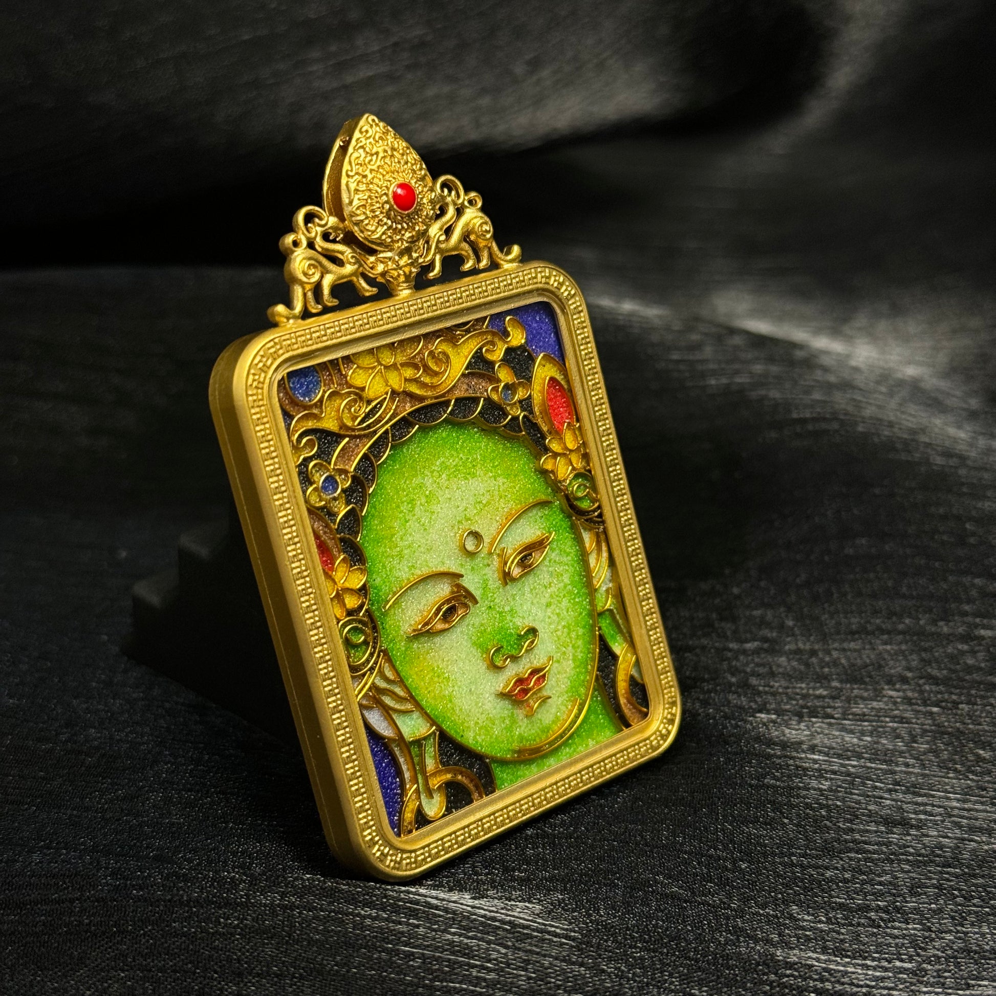 Close angled view of Green Tara mini thangka pendant revealing detailed cloisonné enamel lines, vibrant colors, and gold-plated copper casing.