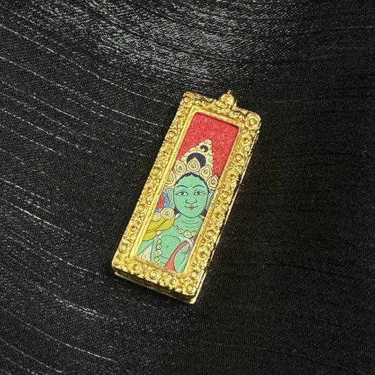 Front view of a Green Tara mini thangka pendant featuring a calm green face, detailed crown ornaments, red background, and a gold-tone raised decorative border surrounding the painting in a slim rectangular pendant form.