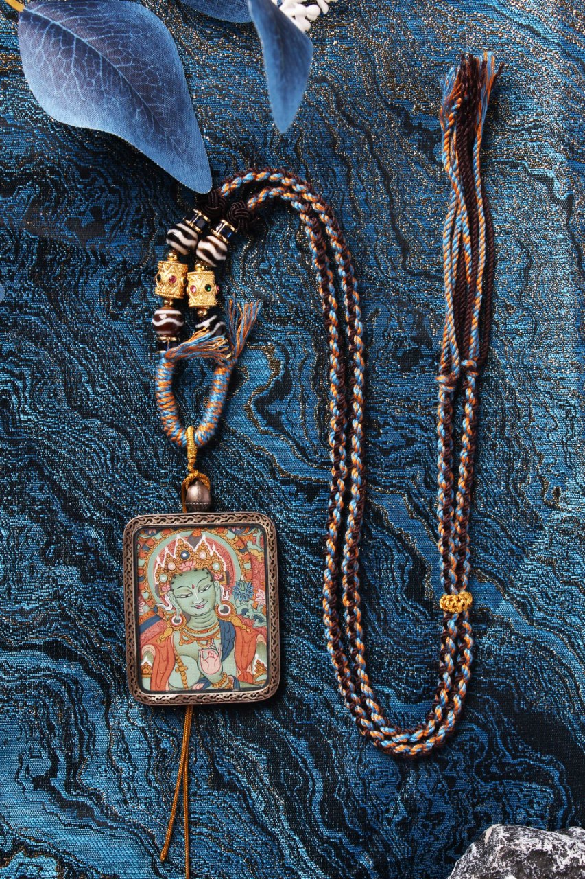 Full display of Green Tara mini thangka pendant necklace with braided cord, beads, and front painting on a blue textile background