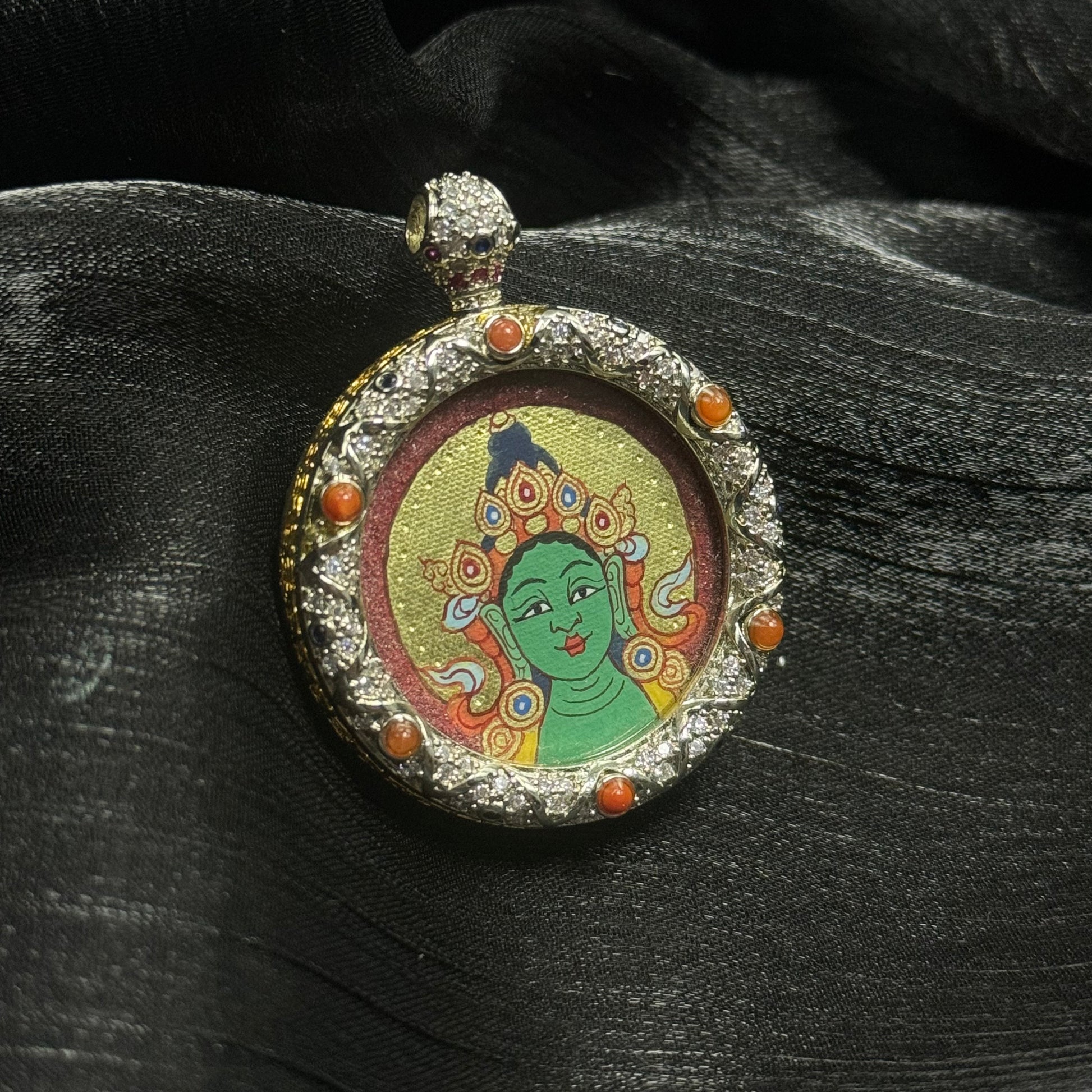 Hand-painted Green Tara mini thangka pendant featuring a vermilion cinnabar background and gold halo, set in an ornate jeweled copper pendant frame with coral-colored stones, traditional Rebgong mineral pigment Tibetan thangka artwork.