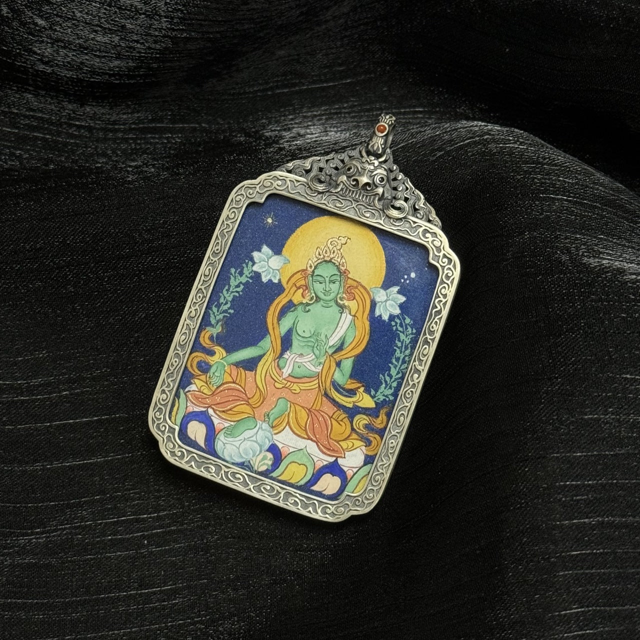 Close view of Green Tara thangka pendant emphasizing coarse mineral pigment layers, halo detailing, and traditional Tibetan color composition.