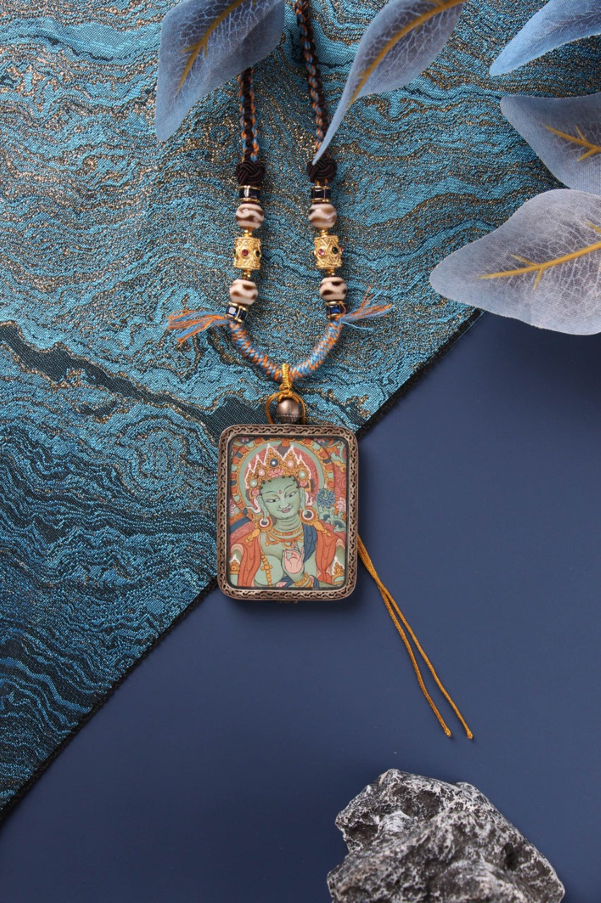Green Tara mini thangka pendant necklace with braided cord and beads, shown front view in a Dunhuang Nine-Color Deer sterling silver case on a blue background