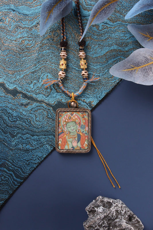 Green Tara mini thangka pendant necklace with braided cord and beads, shown front view in a Dunhuang Nine-Color Deer sterling silver case on a blue background