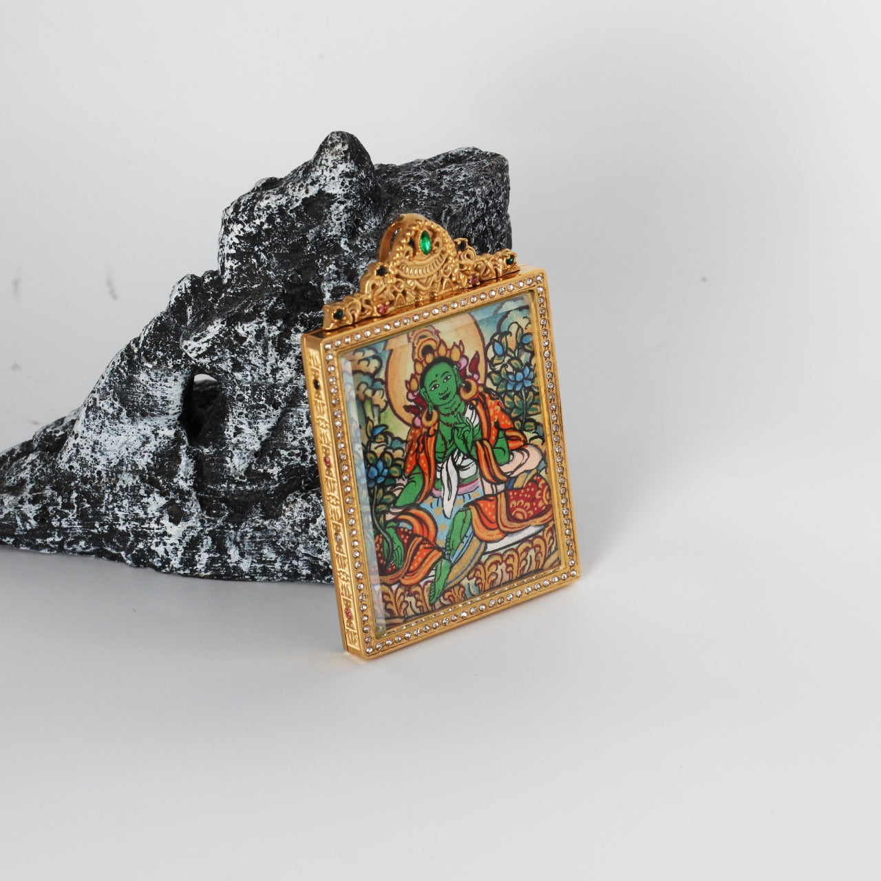 Side-angled photo of Green Tara mini thangka pendant showing the gold-tone titanium steel case profile, crystal border around the front window, and the hand-painted Green Tara artwork inside.