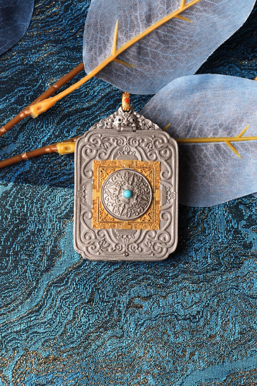 Back side of the Green Tara pendant showing detailed metal relief and central turquoise-colored stone, on a blue textile background