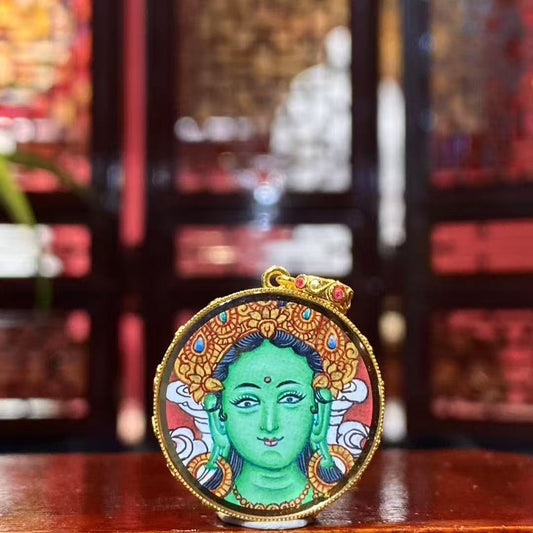 Front view of a round double-sided Green Tara Thangka pendant, hand-painted with 18K gold in Rebgong tradition, depicting Green Tara holding the utpala lotus.
