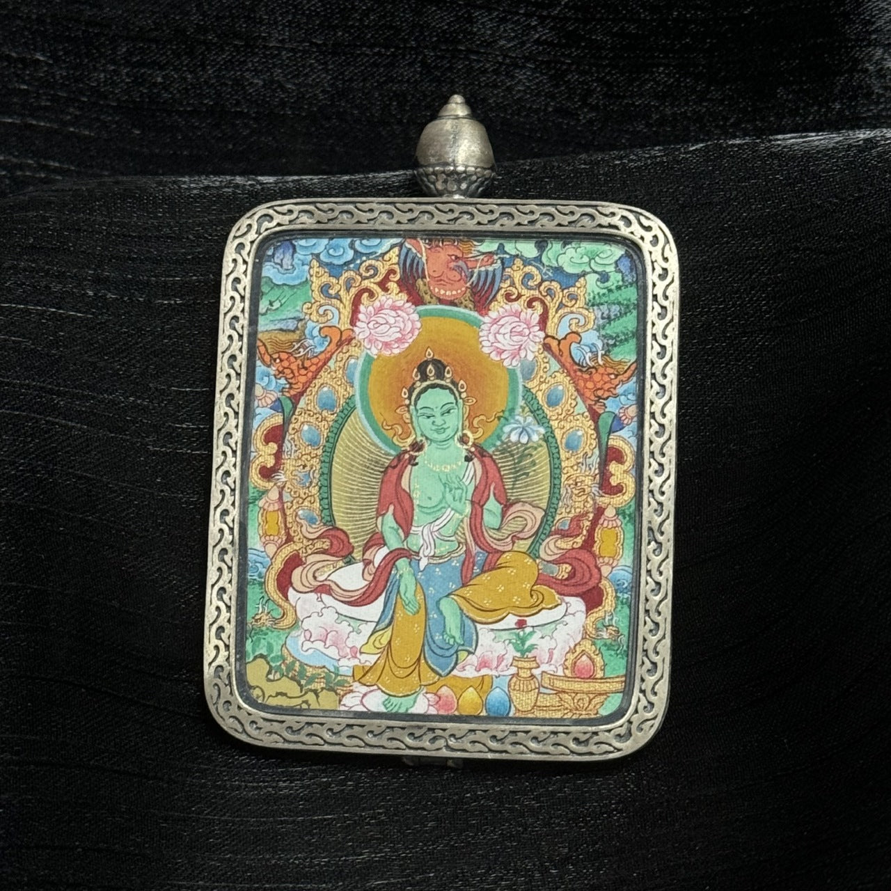 Close-up detail of a Green Tara thangka pendant, highlighting fine line work, vibrant mineral pigments, and traditional Tibetan Buddhist craftsmanship.