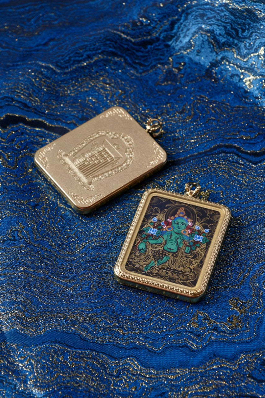 Green Tara mini thangka pendant shown with both front black-gold painting and back-side metal case detail on blue brocade fabric