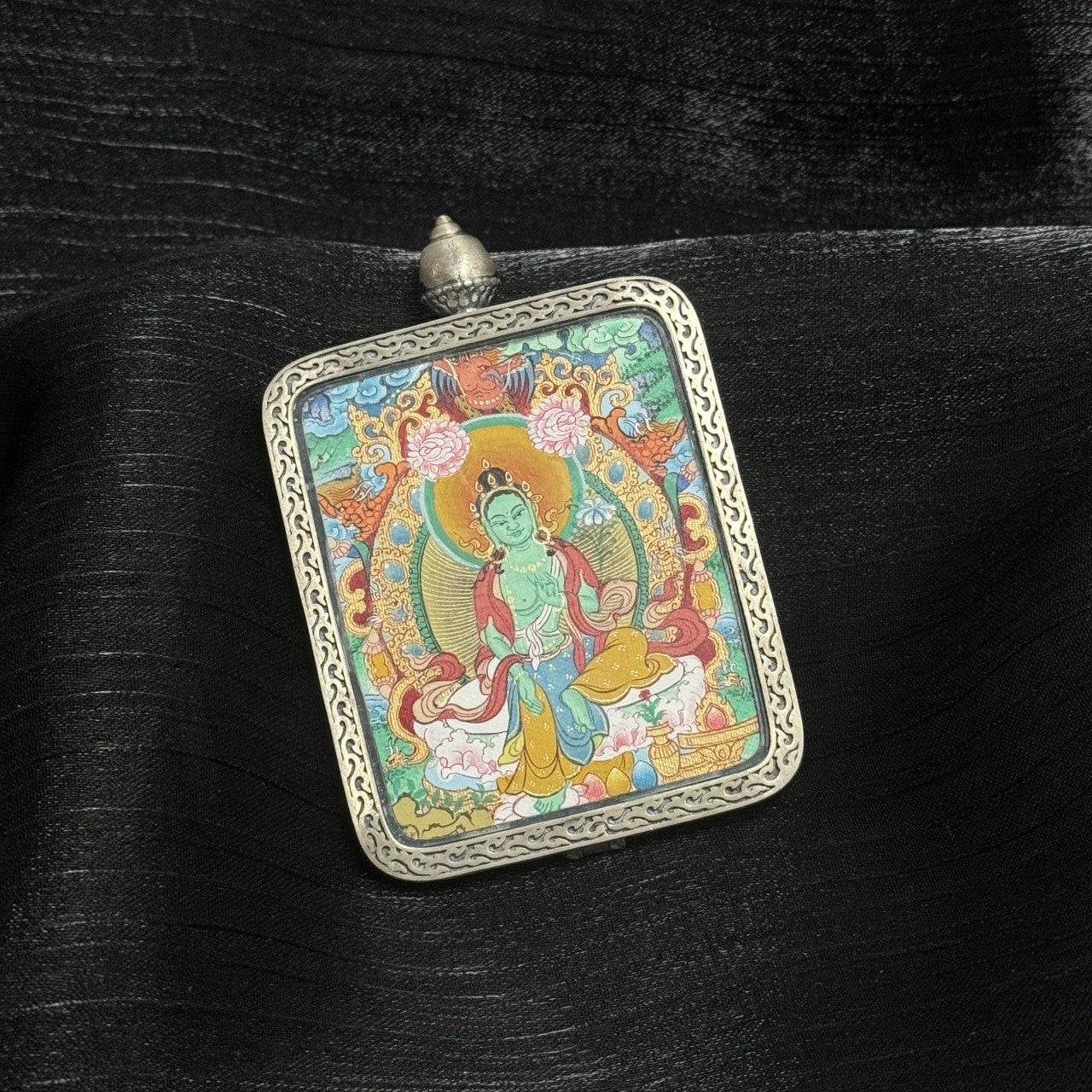 Angled view of a handcrafted Green Tara Tibetan thangka pendant, richly detailed with traditional Buddhist iconography and long-lasting mineral pigments.