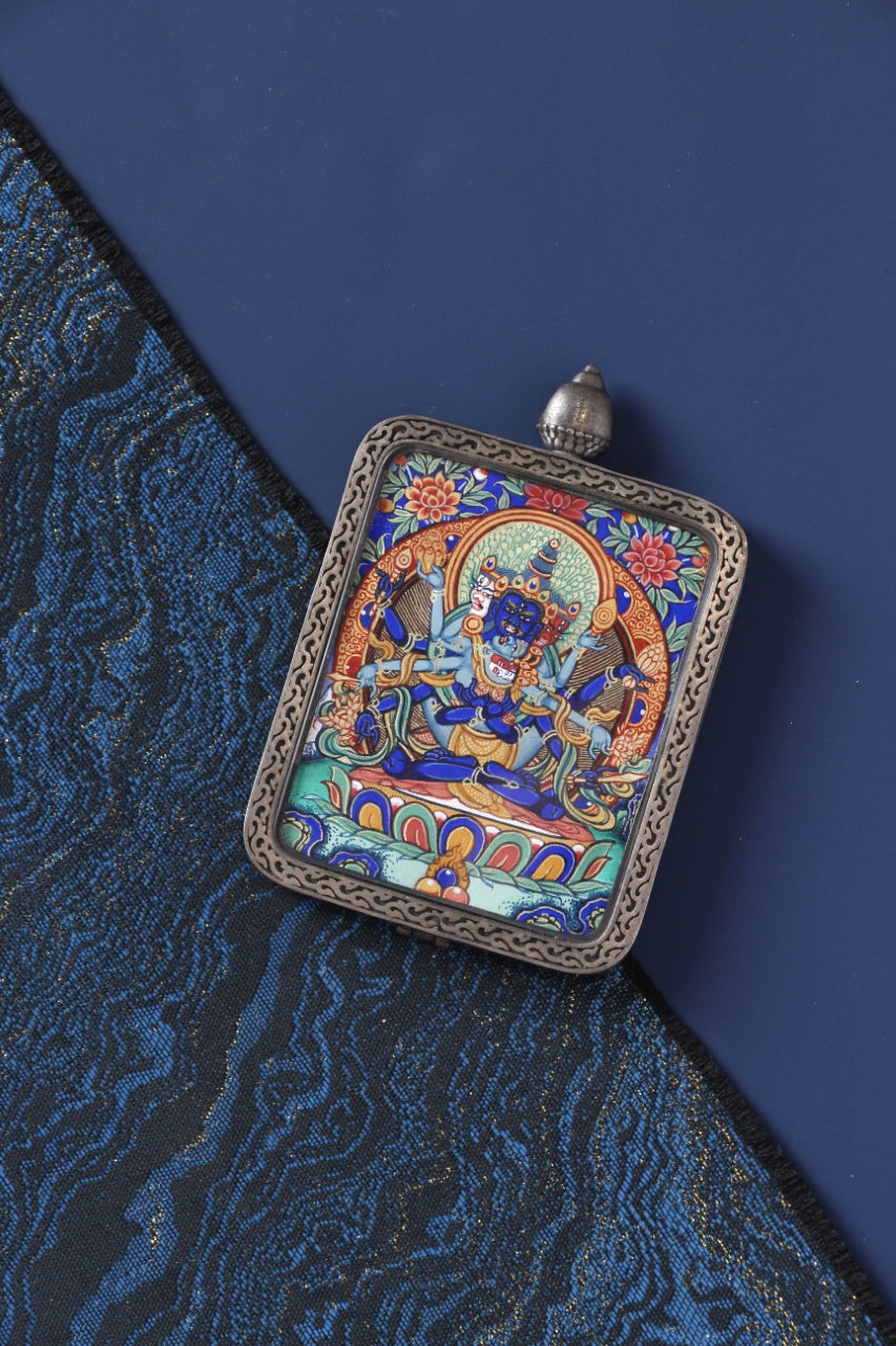 Angled view of a Guhyasamāja Vajra mini thangka pendant, highlighting the protective silver frame, detailed Rebgong-style hand painting, and mineral pigment color layers for a portable Tibetan Buddhist art piece.