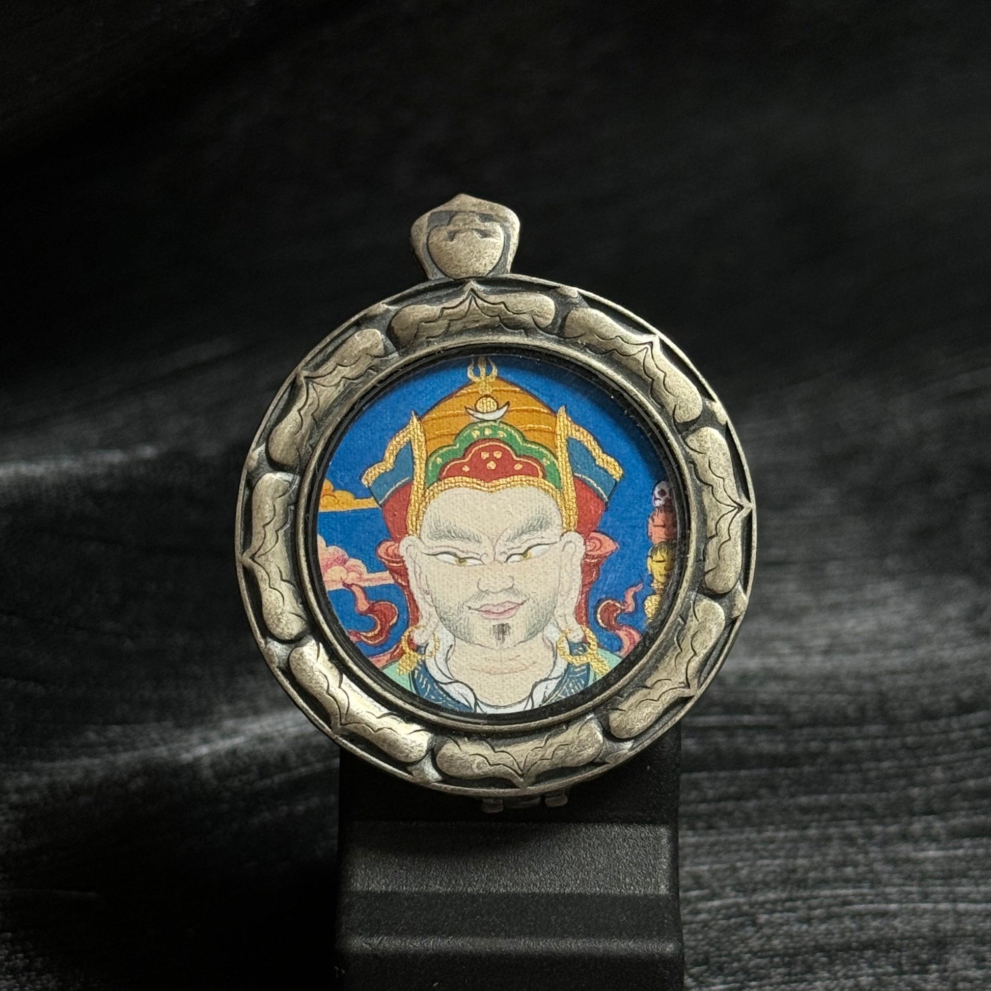 Front view of a Guru Rinpoche mini thangka pendant featuring a circular hand-painted mineral pigment portrait of Padmasambhava inside a carved 925 silver protective frame.