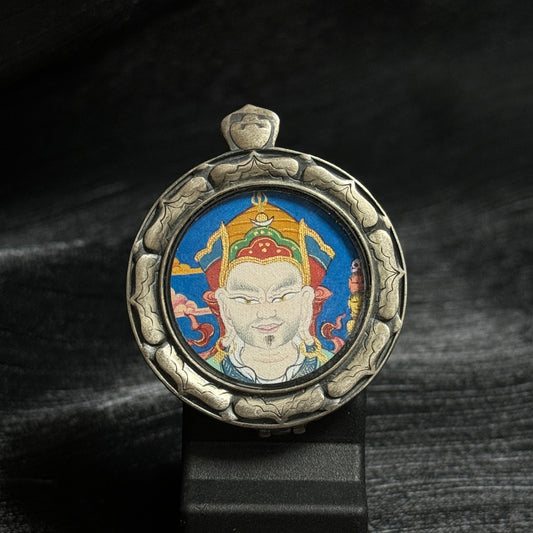 Front view of a Guru Rinpoche mini thangka pendant featuring a circular hand-painted mineral pigment portrait of Padmasambhava inside a carved 925 silver protective frame.
