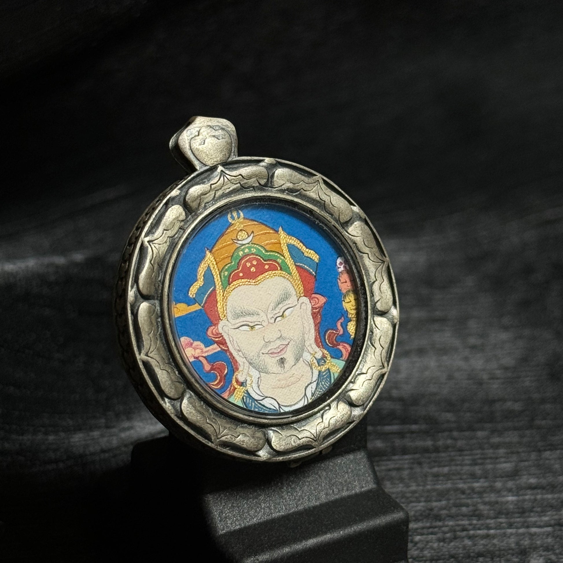 Angled view of the Guru Rinpoche mini thangka pendant showing detailed mineral pigment painting of Padmasambhava and the carved 925 silver pendant case.