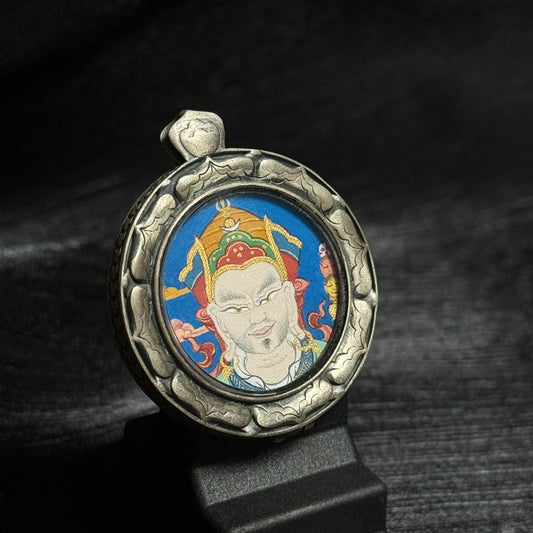 Angled view of the Guru Rinpoche mini thangka pendant showing detailed mineral pigment painting of Padmasambhava and the carved 925 silver pendant case.