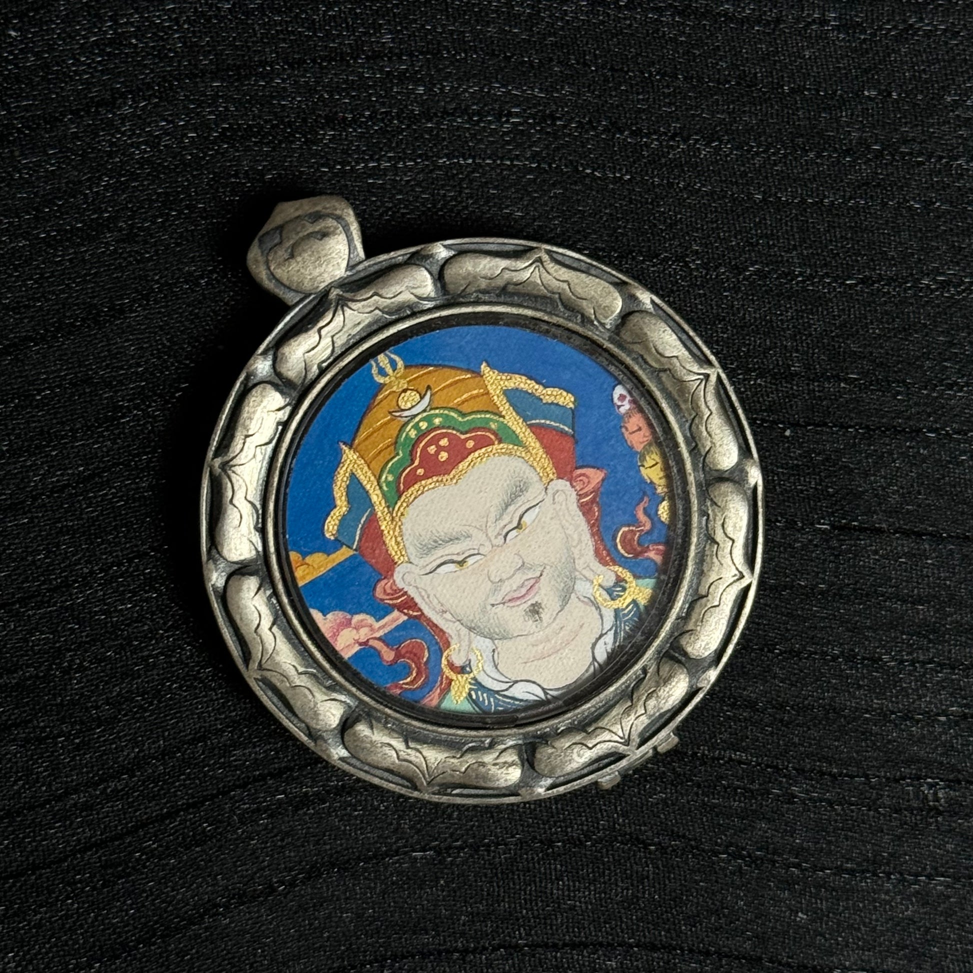 Side-angle view of the Guru Rinpoche mini thangka pendant showing the circular silver protective frame and hand-painted mineral pigment thangka artwork.