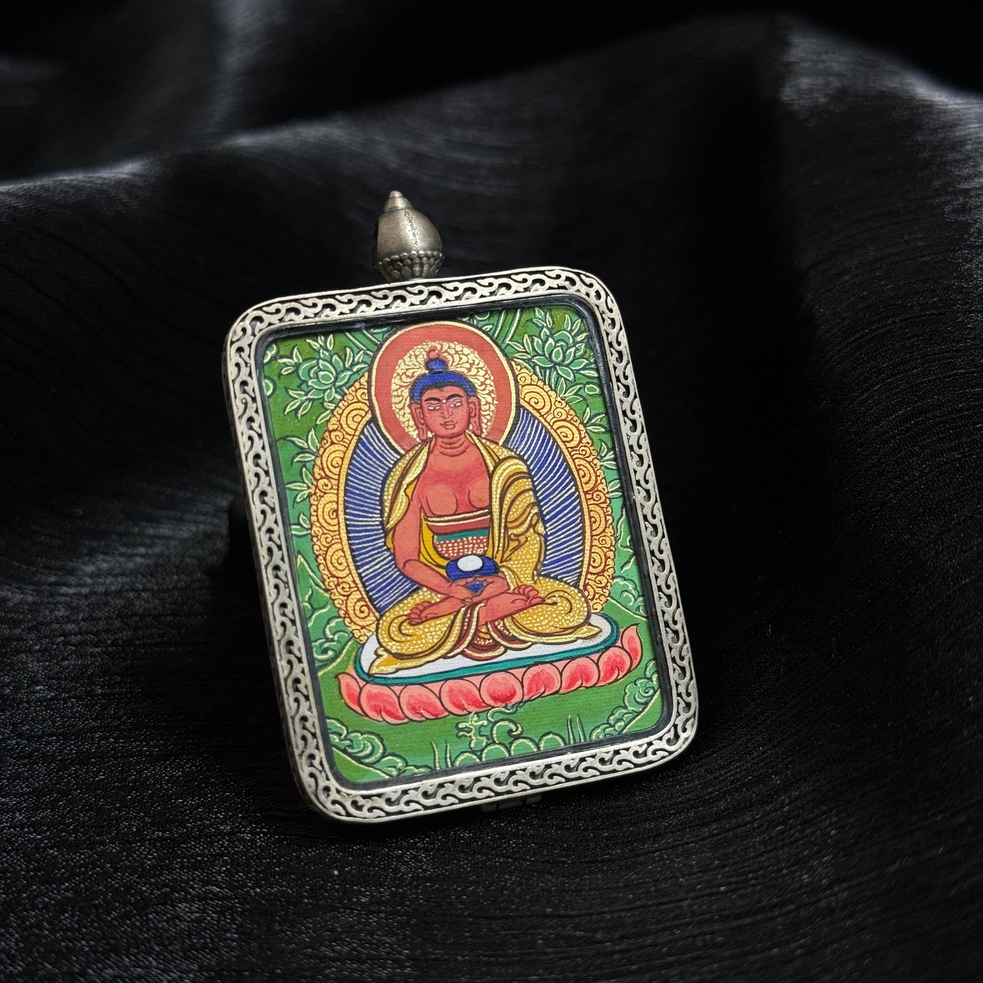 Close angled perspective of Amitabha Buddha mini thangka pendant emphasizing lotus throne detail, precise linework and vibrant mineral pigment colors