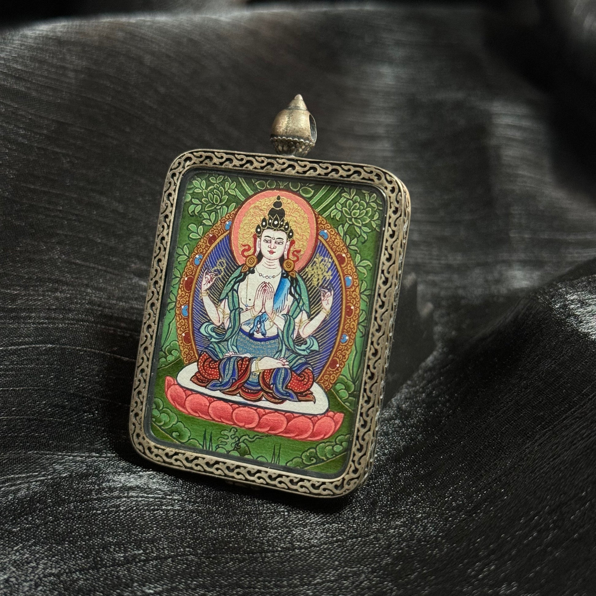 Angled view of Four-Armed Avalokiteshvara mini thangka pendant showing mineral pigment colors and traditional Tibetan thangka iconography