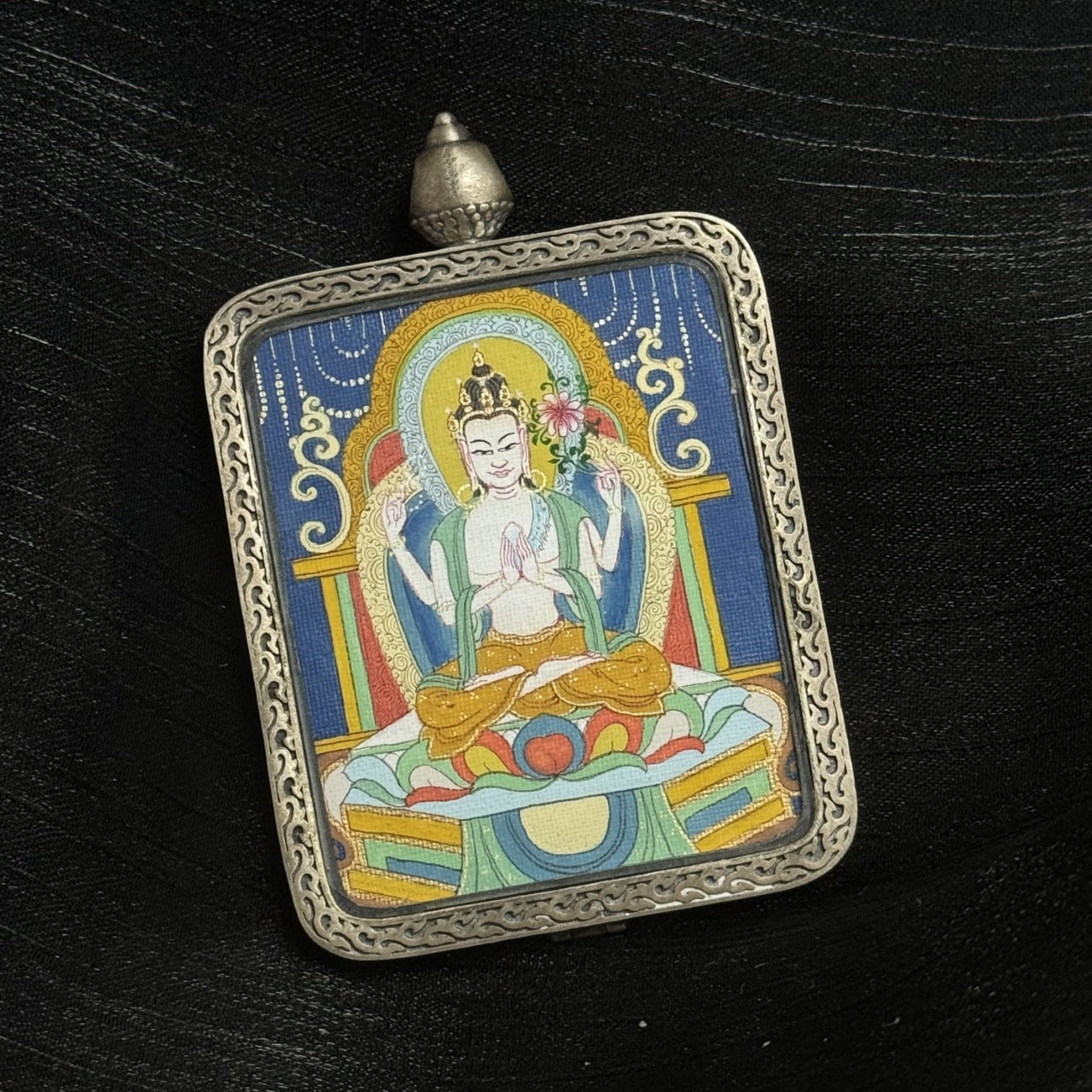 Front view of Four-Armed Avalokiteshvara mini thangka pendant highlighting traditional Tibetan mineral pigment painting and engraved silver protective gawu case