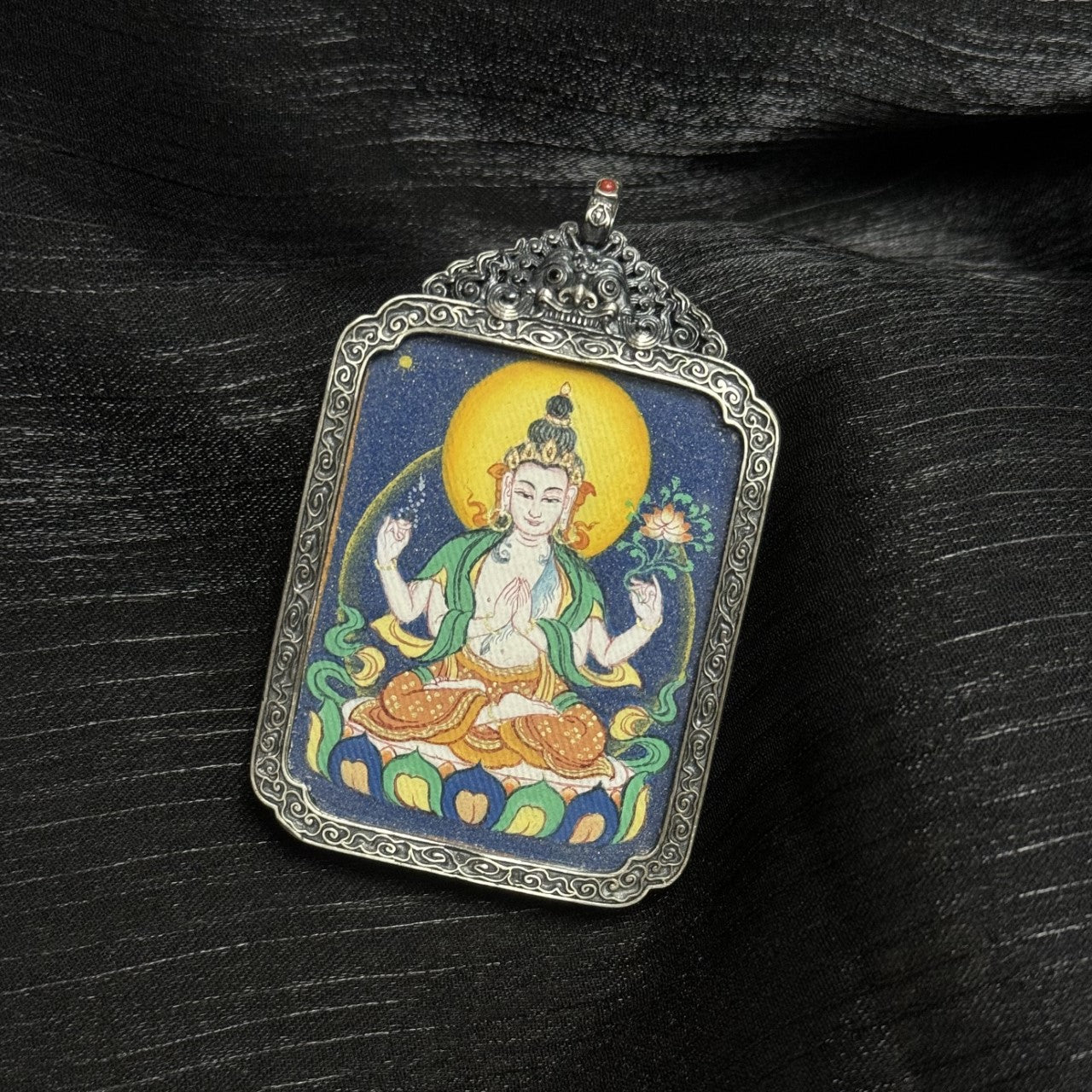 Close-up of Four-Armed Avalokiteshvara thangka pendant highlighting mineral pigment layering, flowing silk ribbons, lotus base details, and antique silver frame craftsmanship.