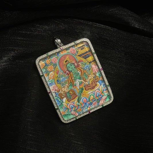 Close-up of a hand-painted Green Tara mini thangka pendant showing the compassionate bodhisattva seated on a lotus throne surrounded by floral patterns and Tibetan architectural elements.