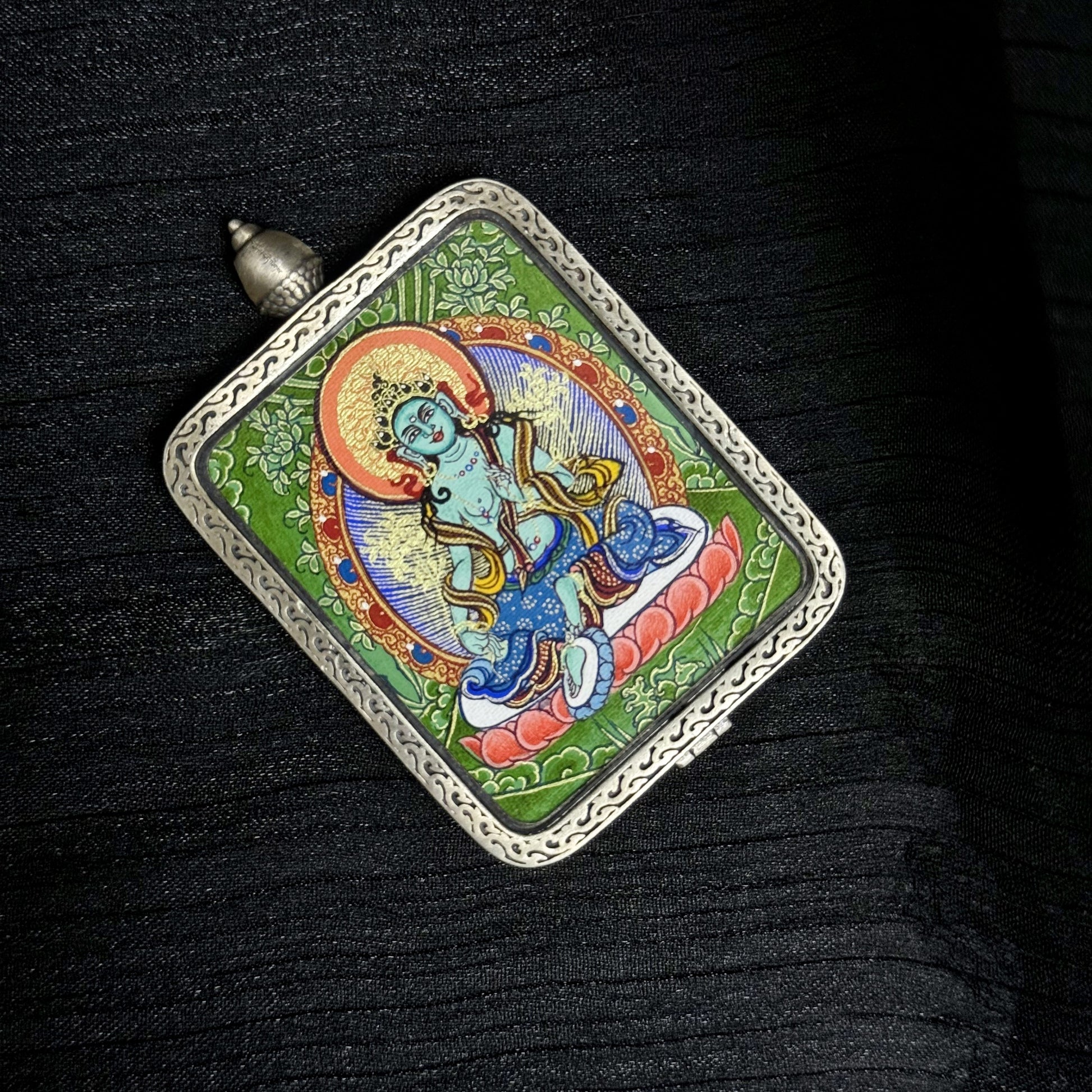 Top angle view of Green Tara mini thangka pendant showing mineral pigment colors and traditional Tibetan iconography within a silver frame